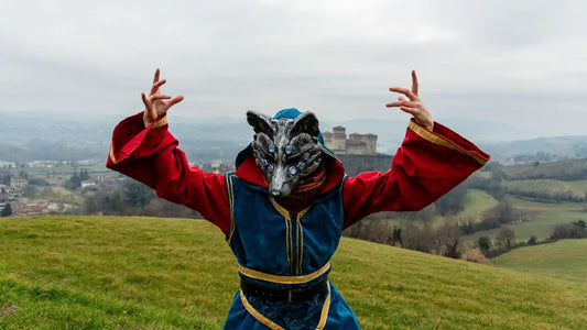 Person wearing a Huli Jing fox mask in a LARP costume on a hilltop with medieval castle in the background.