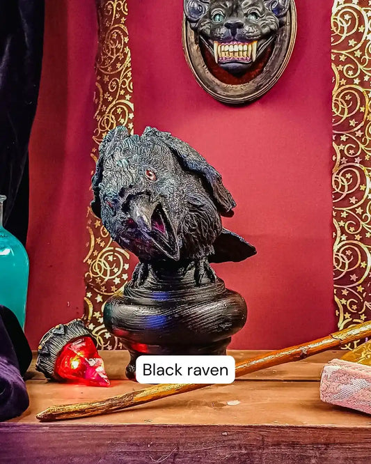 Detailed view of the handmade black raven sculpture with red glass eye, sitting on a wooden base under gothic wall decor and mystical LARP accessories.
