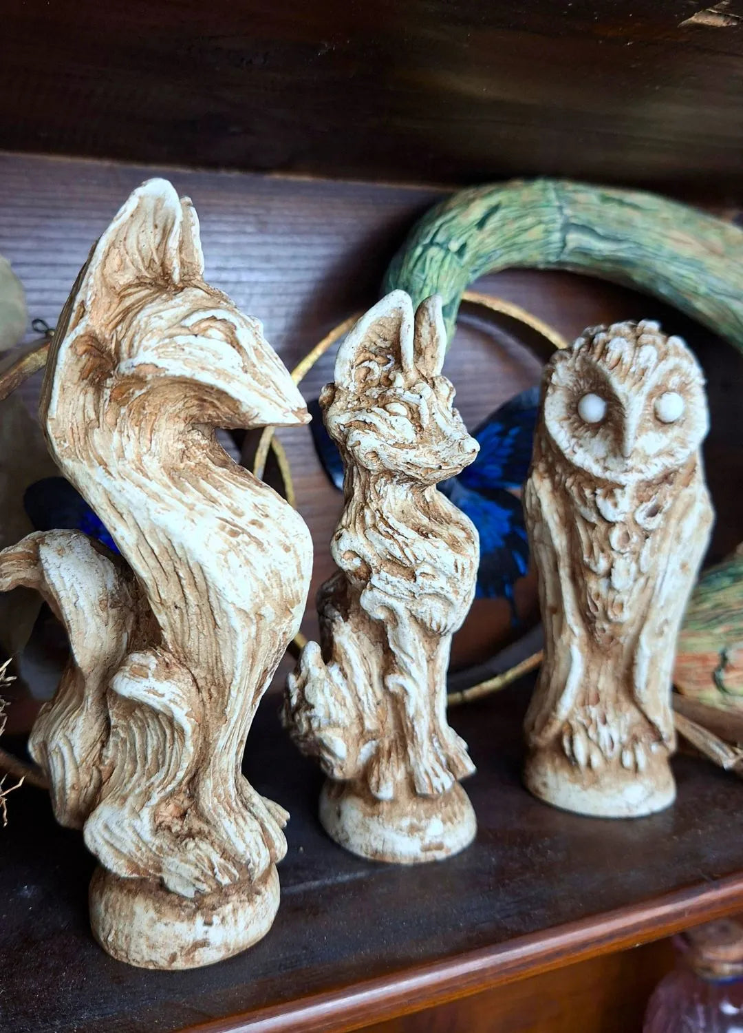 A group of handmade ancient-style resin idols designed as archaeological relics displayed on a dark wooden shelf for cabinet of curiosities decor.
