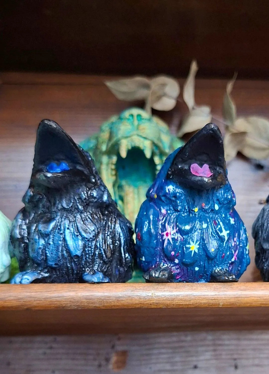 Two small handmade raven statues side by side, one in textured black and one featuring a colorful space galaxy paint variant with stars.
