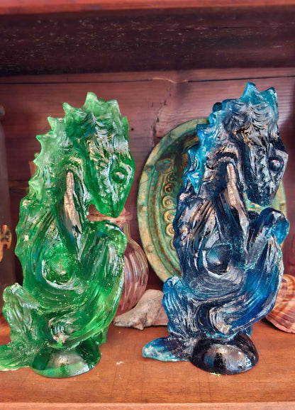 Two translucent resin Dagon Idols side by side, one pigmented in emerald green and one in deep ocean blue, showing sea glass reflections.