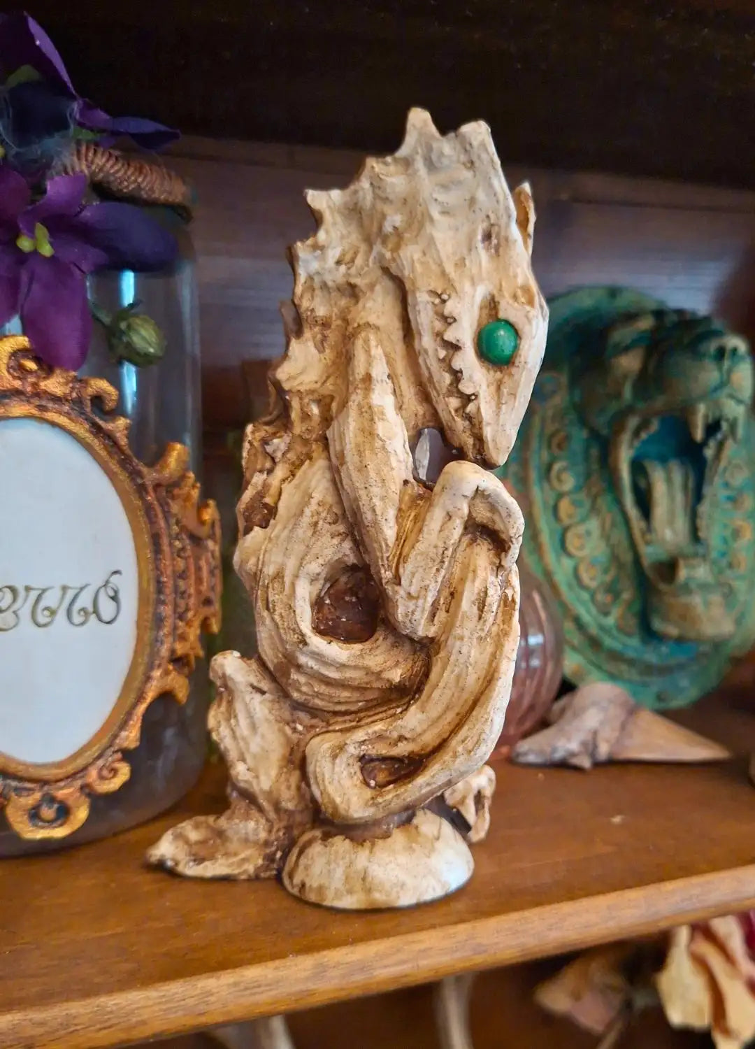 Front view of the Dagon Idol resin sculpture with a weathered antique bone finish and green eyes, displayed on a wooden shelf.