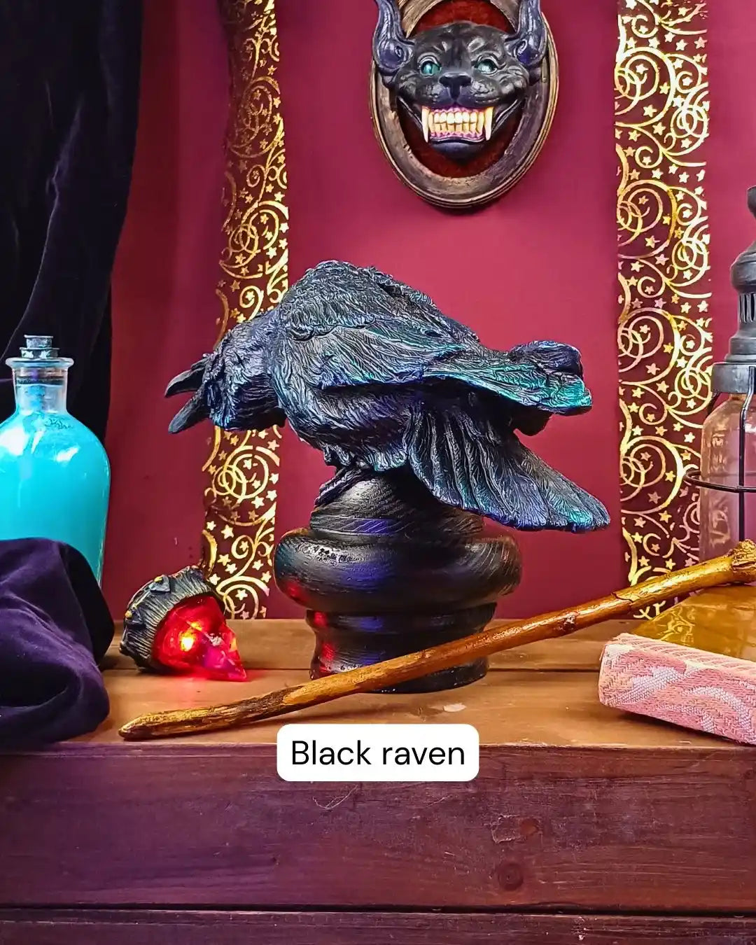 Side view of a sculpted black crow with a dynamic pose, displayed among mystical props and golden gothic wall decor.