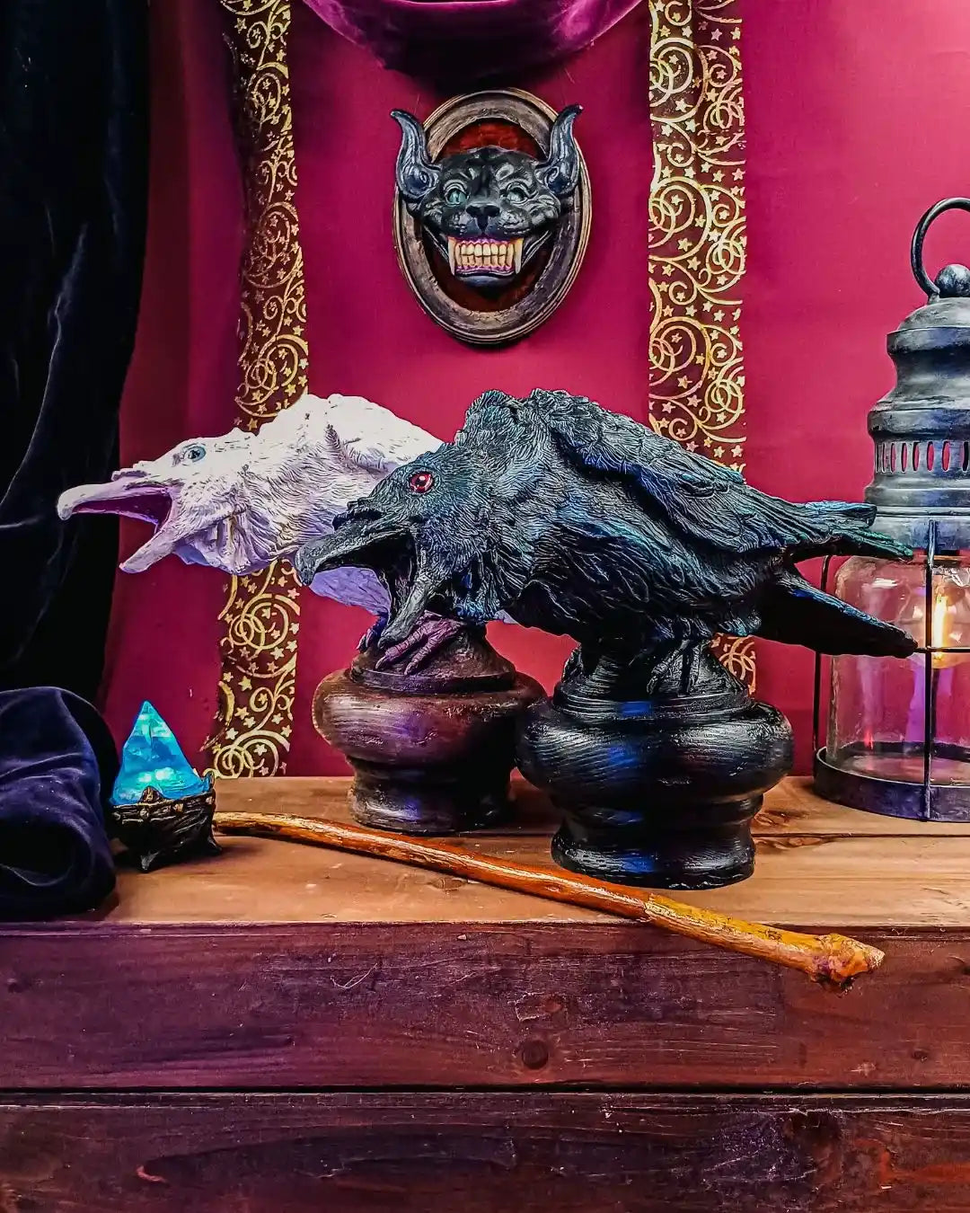 Two handcrafted resin raven sculptures—black and albino—perched on dark wooden bases, styled with gothic props and arcane decor in a wunderkammer setting.