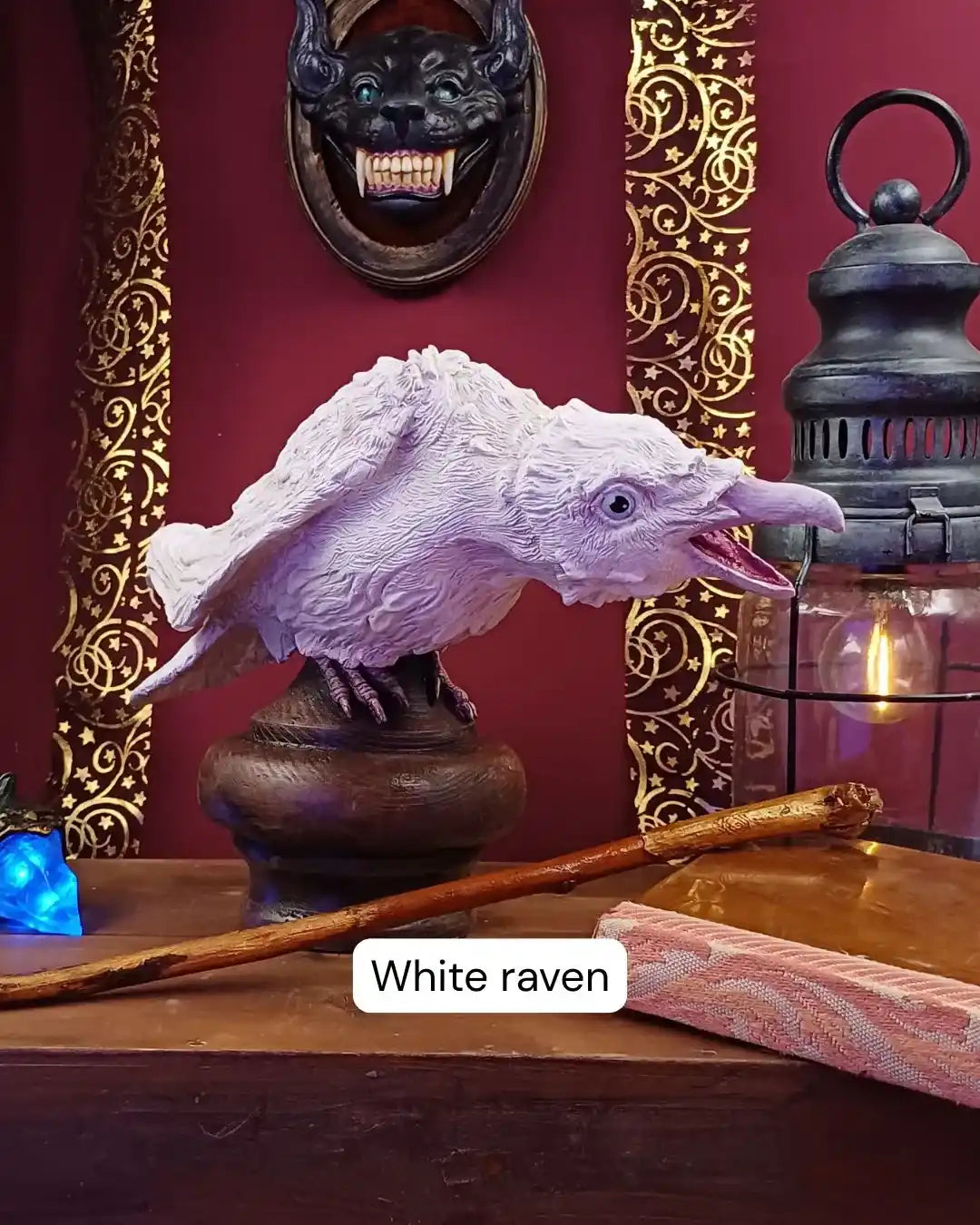 Ivory-colored albino raven statue with soft pastel highlights, resting on a dark wood stand—ideal for esoteric decor, fantasy collectors, and dark academia fans.